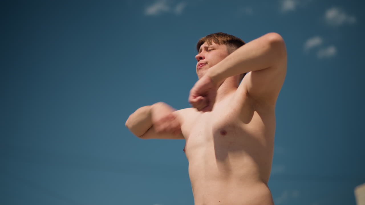 Мужчина занимается боксом на открытом воздухе: молодой человек проводит тренировку по теневому боксу на улице в ясную погоду, любитель фитнеса выполняет упражнения по теневому боксу на открытом воздухе при ярком солнечном свете и с городскими зданиями на заднем плане