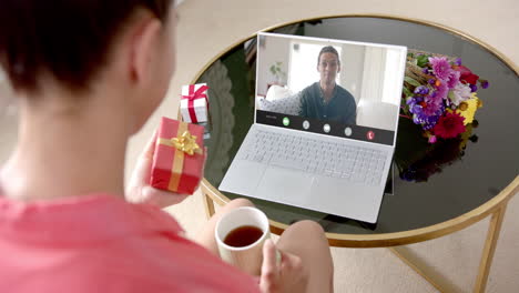 caucasian man holding gift and talking with caucaslan woman on laptop screen