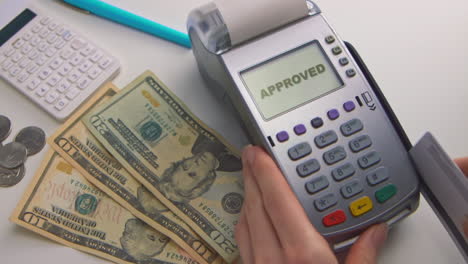 a woman's hand swipes a card into a debit machine