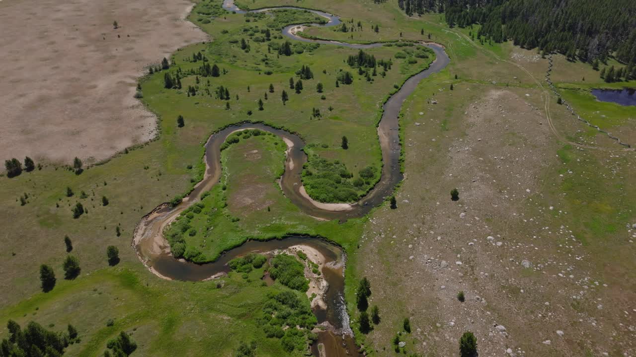 Aerial high angle overview of meandering winding rivers and green plains in the Big Sandy Trailhead of Wind River Wilderness, Wyoming, with mountain views