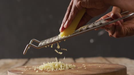 Video-close-up-of-hands-of-african-american-man-grating-cheese-onto-wooden-board-on-rustic-table