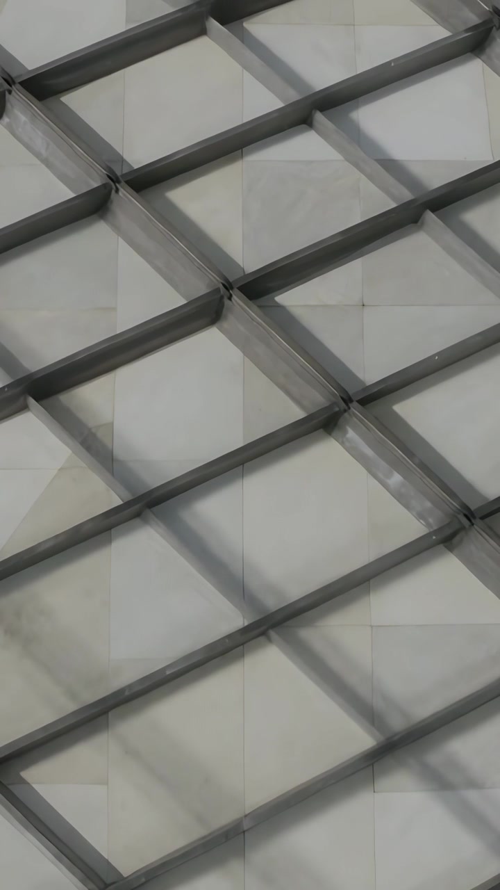 Video verticale: Telecamera in panoramica che mostra un reticolo metallico con saldature che proietta ombre mutevoli sul soffitto.