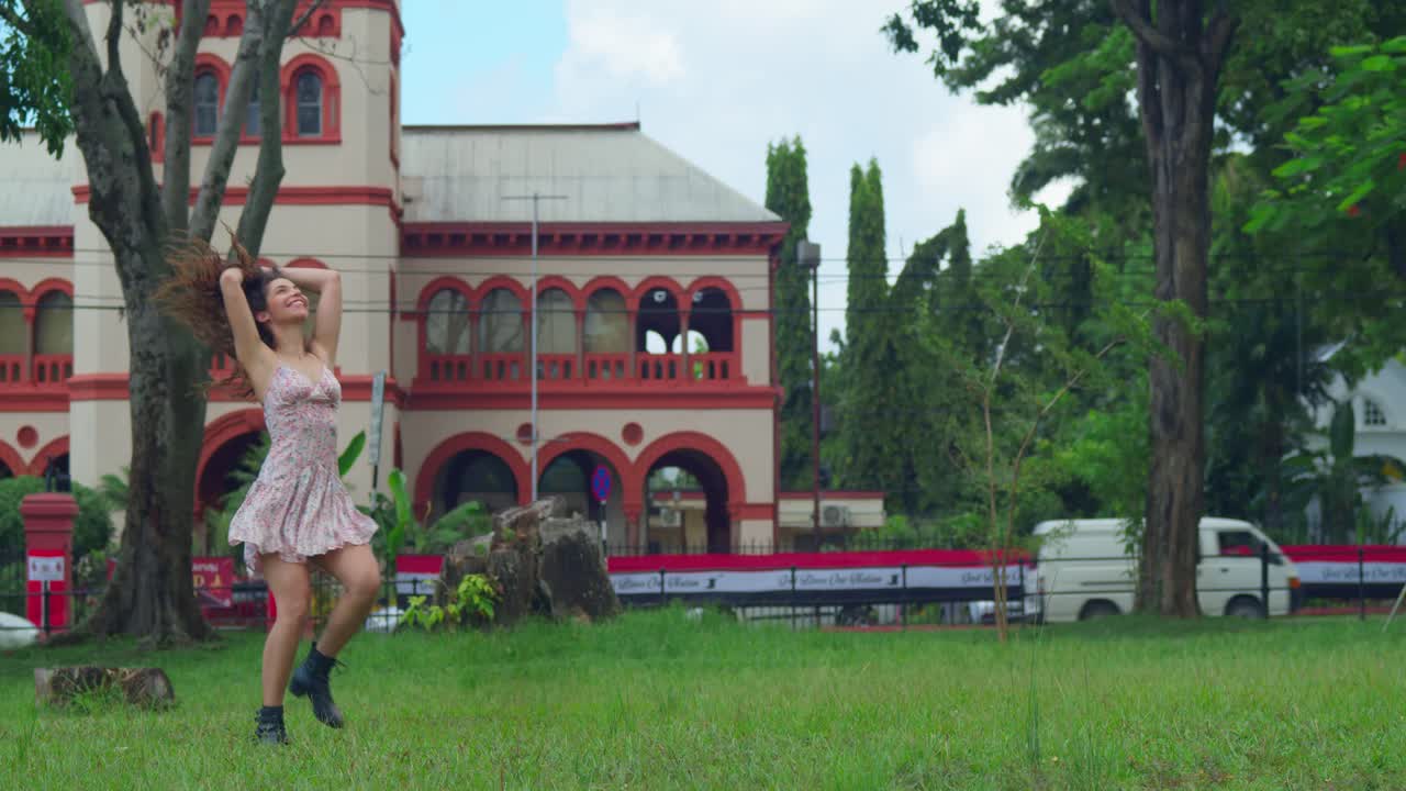 젊은 여자가 뒤에 성이 있는 공원에서 미니 드레스를 입고 회전하고 춤을 춘다.