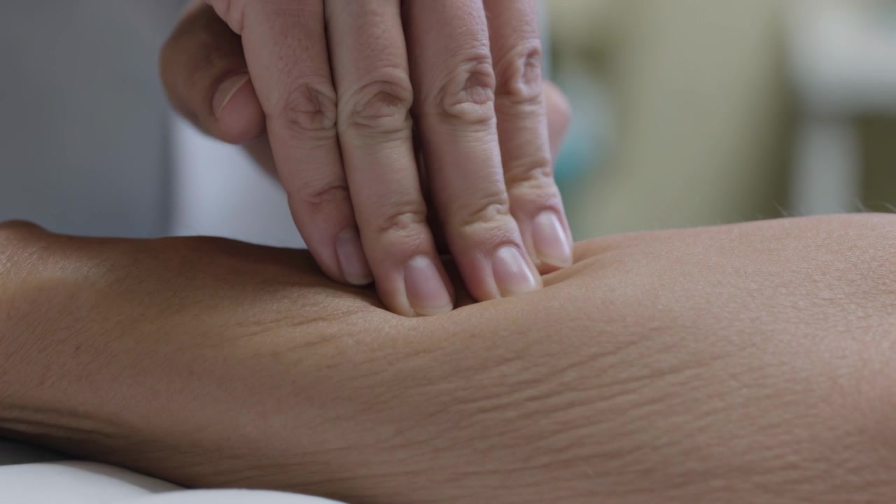 Terapista in bianco che posiziona le mani, applicando una pressione più decisa sull'avambraccio del cliente in clinica, durante la valutazione.