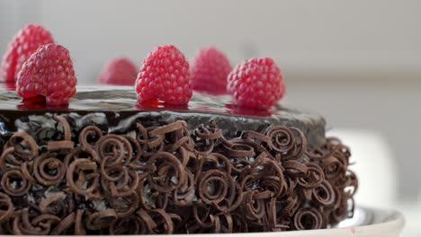 close up shot of chocolate cake topped with raspberries and garnished chocolate spirals rotating clockwise