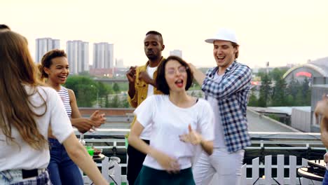 pretty young woman and her joyful friends are dancing on rooftop celebrating holiday and enjoying good company. summertime, leisure and hobby concept.