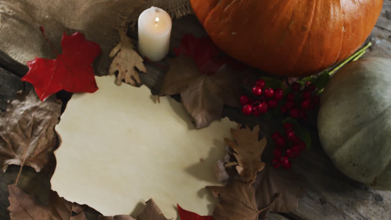 Paper with copy space against autumn leaves, candle and pumpkins on wooden surface