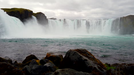 Godafoss-Icelandic-Waterfall-low-pan-and-dolly-across-rocks-4k-ProRezHQ,-Beautiful-12-meter-39-feet-high-horseshoe-shaped-crystal-clear-cascade-on-the-river-Skjálfandafljót-in-northern-Iceland