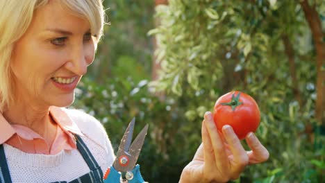 mujer madura sosteniendo tomate y tijeras de poda