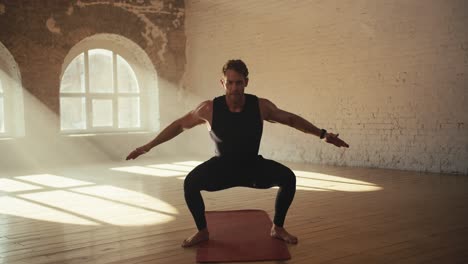 athletes man black sports tight in uniform crouched down and waving his arms. morning workout and sports in a sunny gym with brick walls