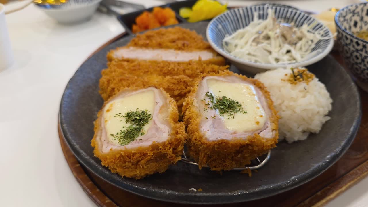 Delicious Japanese tonkatsu set meal, featuring crispy cheese-filled and original pork cutlets served with rice and shredded cabbage salad in a restaurant - A parallax shot