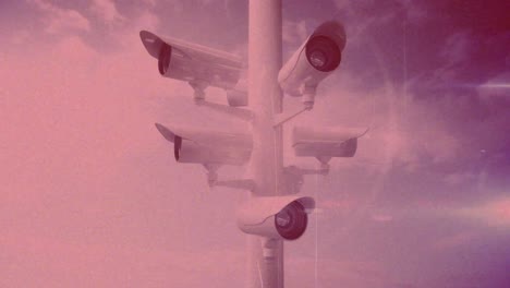 animation of moving cctv cameras over clouds on blue sky with pink tint in the background