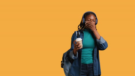 Girl-with-backpack-and-headphones-yawning,-feeling-tired,-studio-background