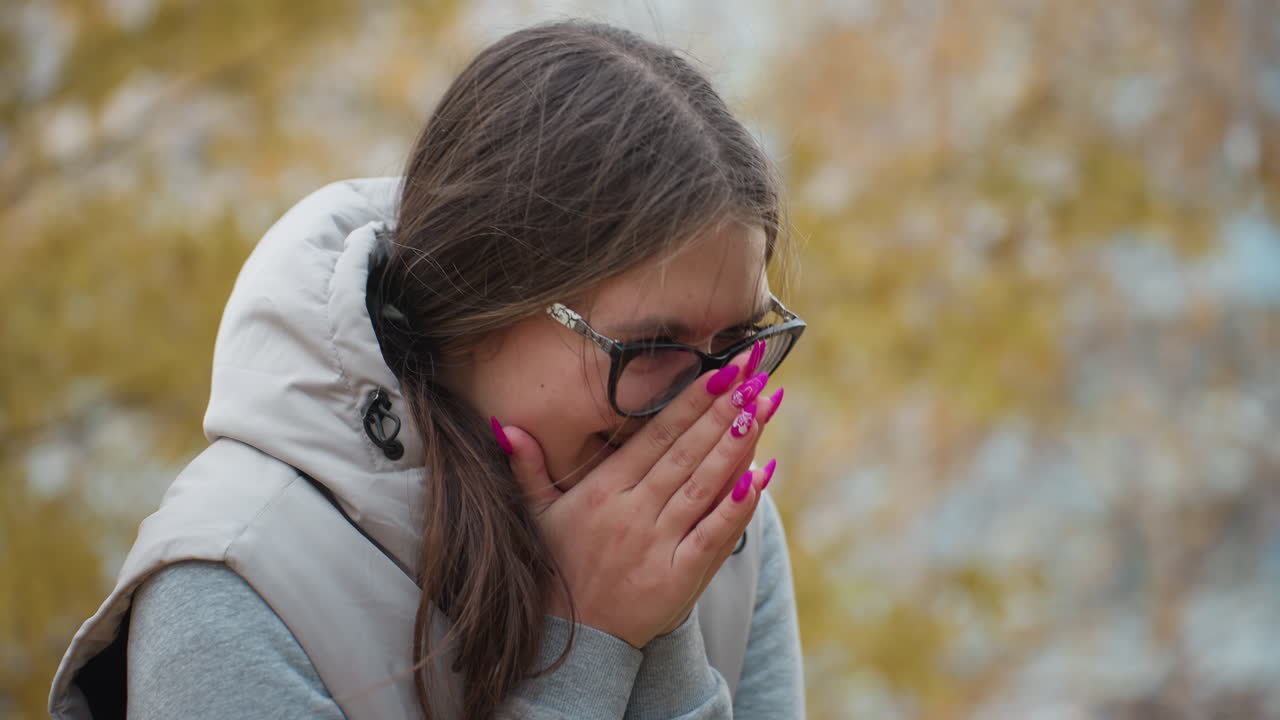 Close up of excited woman in glasses with long hair swaying in autumn breeze smiling softly as she reacts to romantic proposal from man kneeling before her surrounded by warm seasonal colors