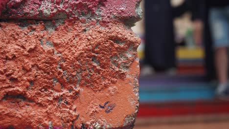 a close up of a red brick wall with graffiti, blurred people in the background