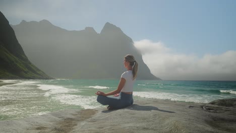 young beautiful blonde meditating on norway coastline, orbiting view