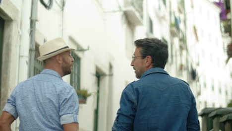 back view of gay couple holding hands, walking streets of city