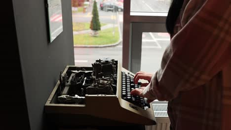 retrato de una persona escribiendo en una máquina de escribir manual antigua junto a la ventana con vehículos que pasan por fuera