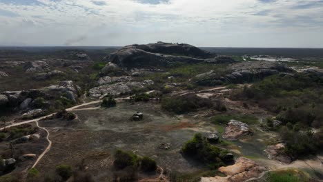 flyover rocky terrain with dirt roads, sparse vegetation and massive granite rocks in chaval, ceara, brazil. dolly in drone aerial