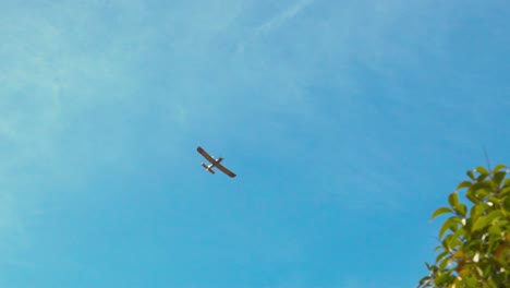 Slow-motion-footage-of-single-engine-training-airplane-,-flying-low-over-the-trees-,-clear-blue-sky-in-the-background