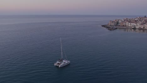 Luftaufnahme-Eines-Bootes-Auf-Ruhiger-See-Mit-Menschen-Bei-Sonnenuntergang,-Cefalu,-Sizilien,-Italien