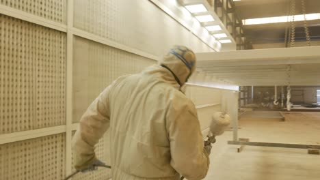 worker paints an iron structure white, paint pressure gun is the tool used in the image. workstation