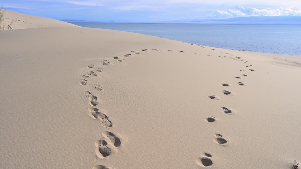 Footprints in the sand create a winding path over a large dune beside Durgun Nuur lake in Mongolia. A metaphor for a journey or finding one's way