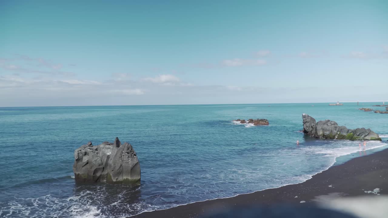 вулканический черный песчаный пляж с купающимися людьми