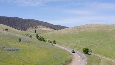 beautiful tracking shot taken from above, car driving through the australian wilderness with some trees and meadows, no people, daylight, sunny day