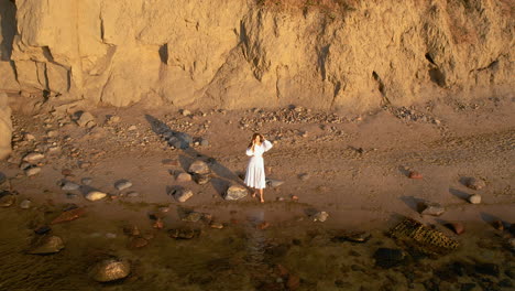 Mujer-Aventurera-Con-Vestido-Blanco-Disfruta-Del-Amanecer-De-Pie-Junto-A-La-Costa-Rocosa-Con-Acantilados-En-El-Mar-Bastic-Orlowo-Gdynia,-Polonia