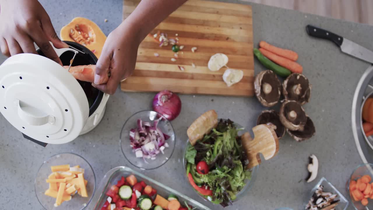 Overhead view of african american woman cooking in kitchen, composting vegetable waste, slow motion