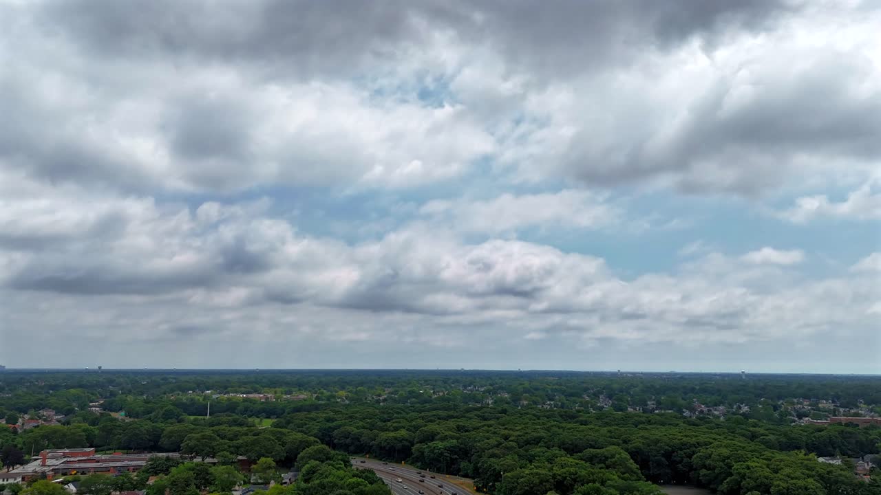 An aerial time lapse over Southern State Parkway on Long Island during a cloudy day. Flying over green trees in the suburban neighborhood. The camera dolly in high up over the landscape