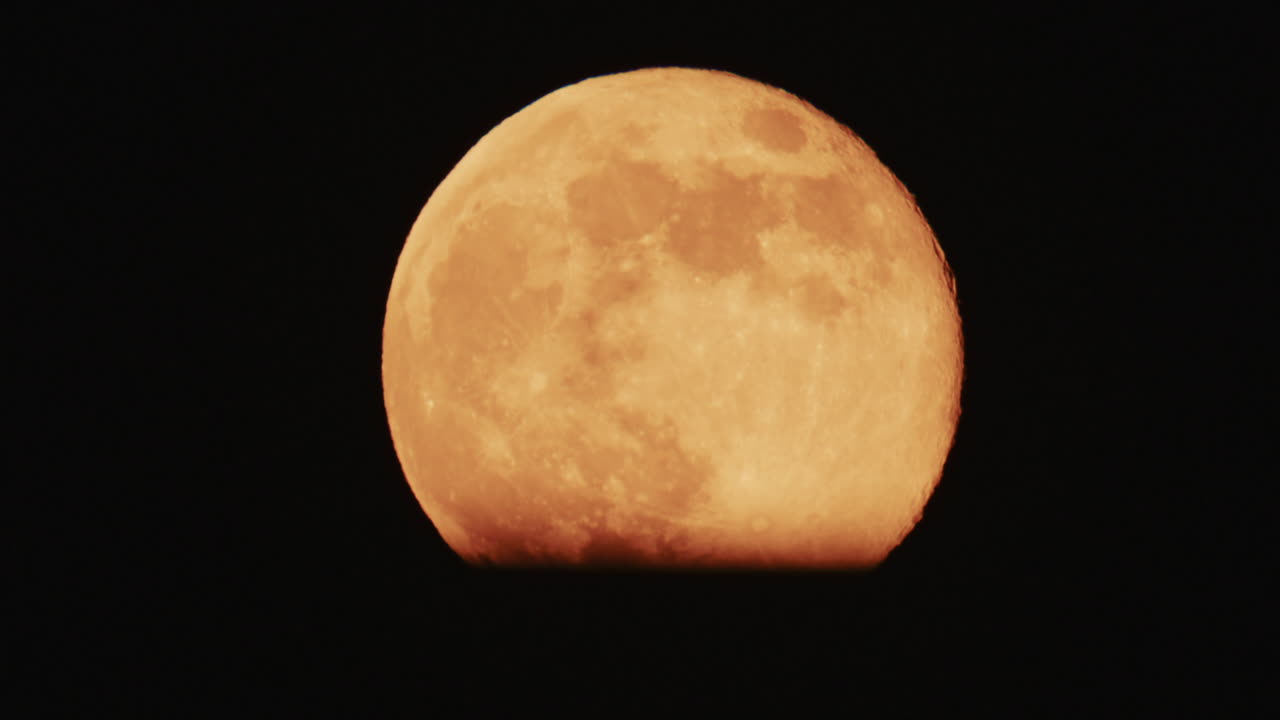Large full moon rising against a dark night sky with clear details and dramatic atmosphere