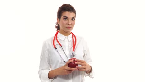 Young-nutritionist-holding-red-apple,-advising-healthy-diet.-Friendly-female-doctor-showing-red-apple-smiling.-Portrait-of-young-professional-with-stethoscope-and-lab-coat-isolated-on-white-background