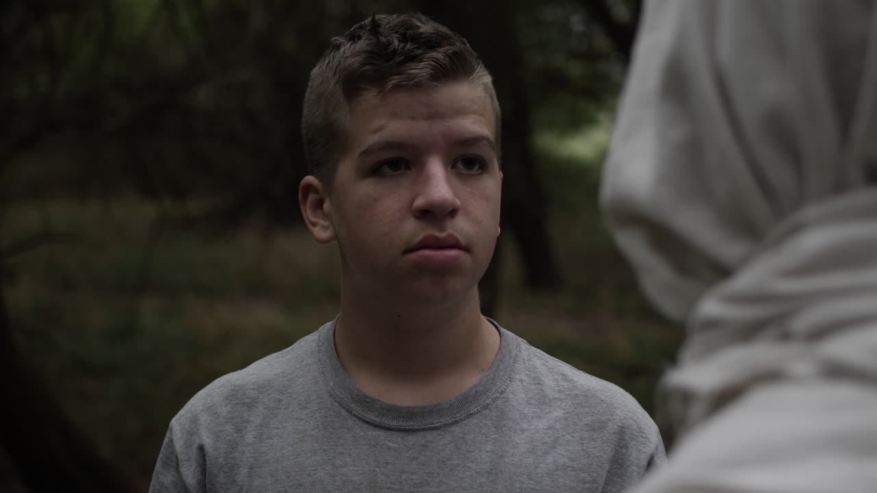 숲에 서 있는 십대 소년은 옷을 입은 남자를 조심스럽게 본다