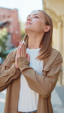 young caucasian woman meditating breathes deeply with hands clasped praying eyes closed on street