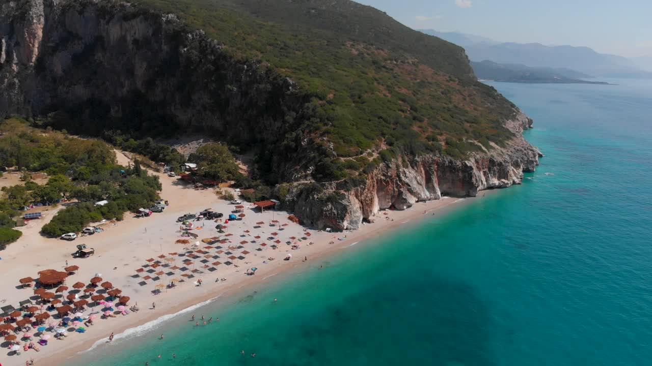 Stunning reveal shot of beautiful Gjipe Beach in Albania with sun umbrellas