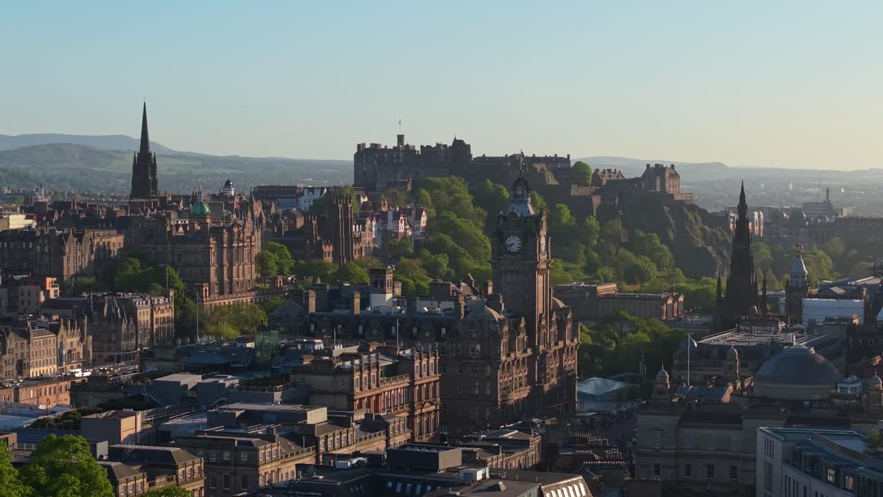 Filmagem cinematográfica suave de drone com movimento paralelo, exibindo o Castelo de Edimburgo, a elegante Torre do Relógio Balmoral e o imponente Monumento a Scott em uma paisagem urbana deslumbrante.