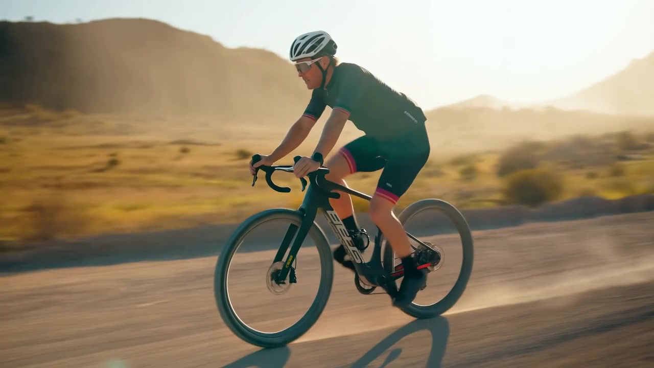 Ciclista in bicicletta, in un paesaggio desertico con montagne sullo sfondo, con bicicletta, strada, con texture della superficie stradale e del terreno montuoso, da una prospettiva laterale del ciclista.