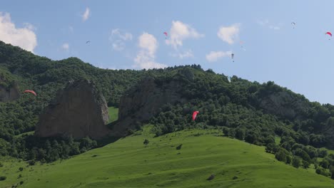 paragliding pilots fly paragliders among clouds and green mountains.