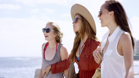 Three-young-women-tourists-on-summer-vacation-walking-on-beach-promenade