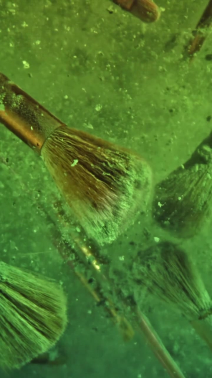 Pennelli da trucco immersi in un liquido verde brillante con particelle galleggianti