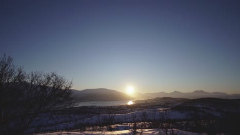 Panning-shot-of-a-winter-landscape-with-the-sun-rising-setting-over-a-city-in-the-distance