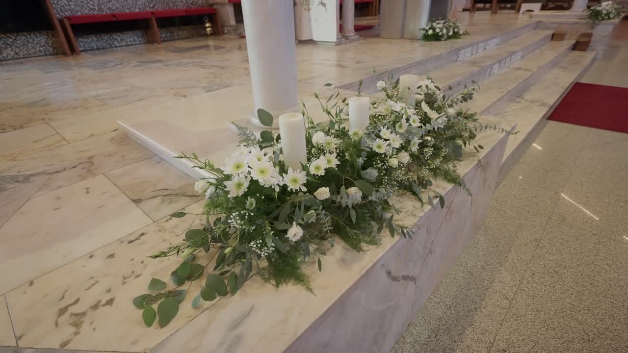 屋内の教会の祭壇階段にある、白いろうそくが置かれた生花飾り。