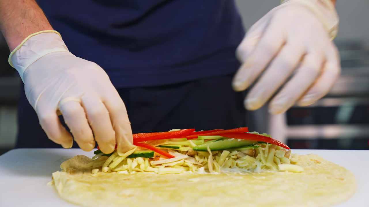 Cooking meal in fast food restaurant. Professional cook in white gloves puts filling with cutted vegetables into pita. Process of cooking tasty snack.