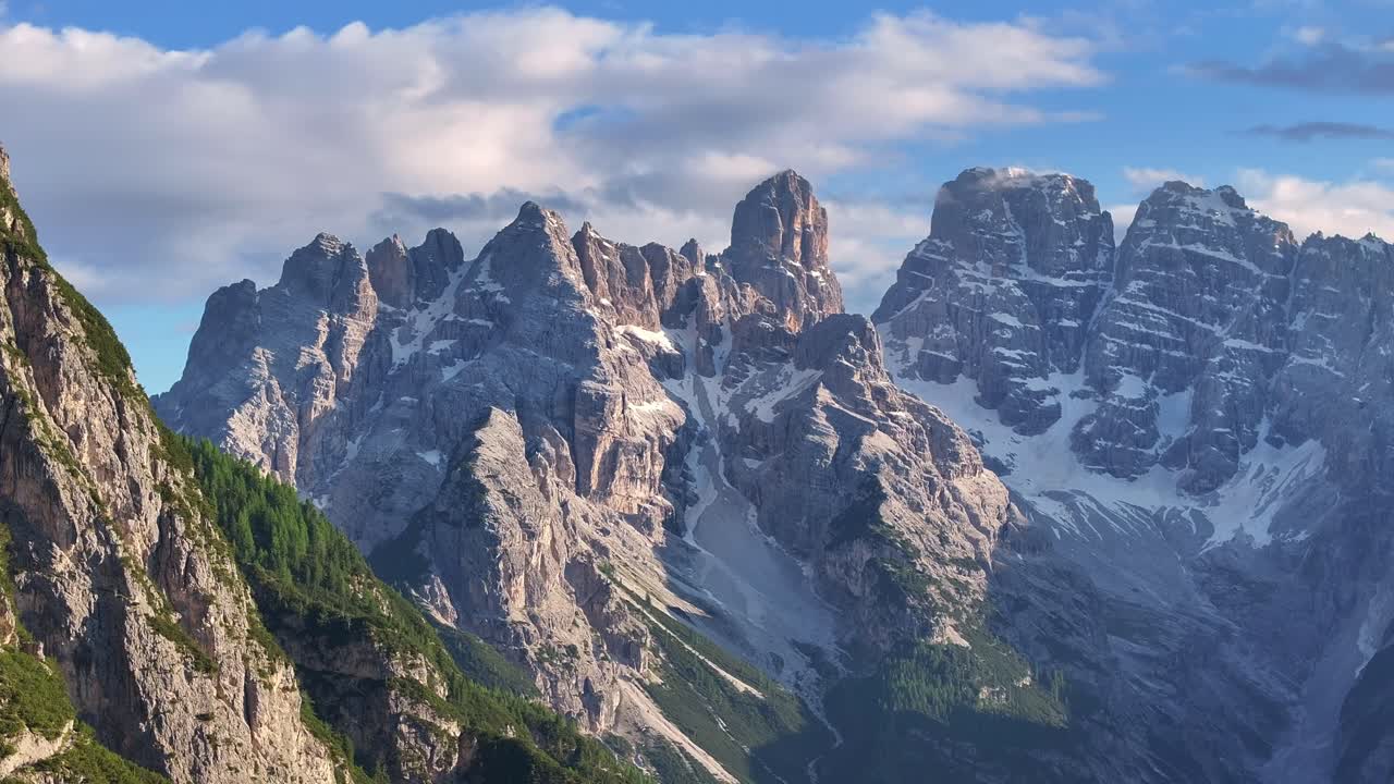 The drone slowly descends sideways from Lago di Landro, revealing dramatic Dolomite peaks under evening light