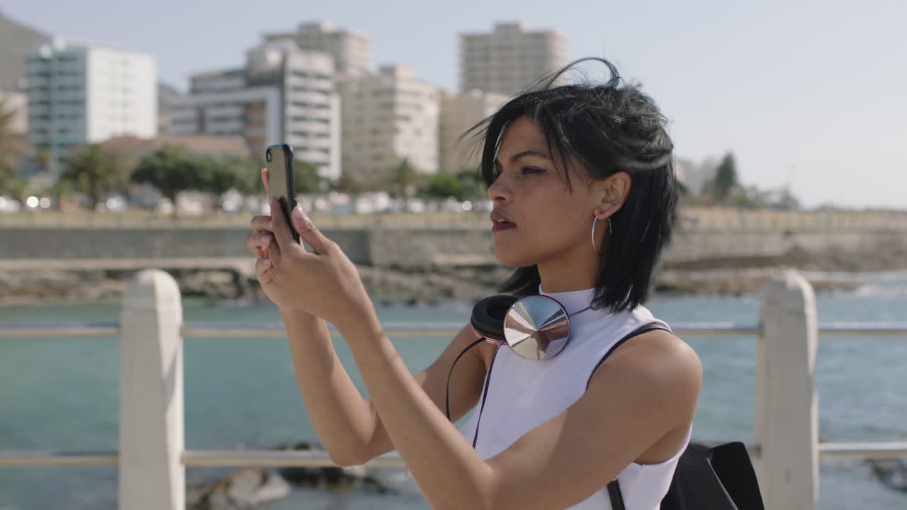 retrato de una joven mujer hispana tomando una foto de la vista de la costa usando un teléfono