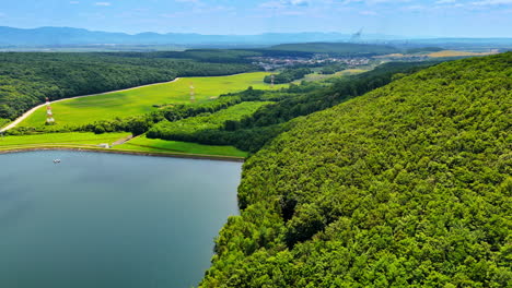 lush green by calm lake. green hills tower over a calm lake beneath a blue sky, framed by distant mountains in a beautiful scene