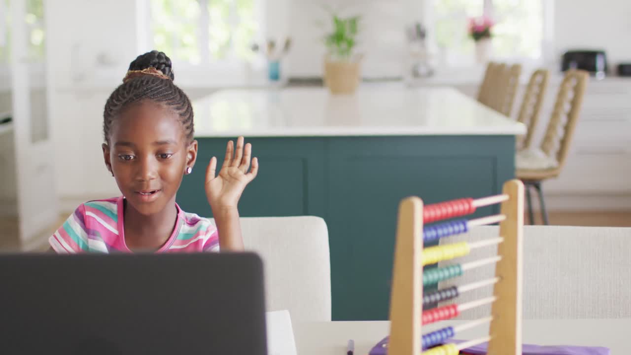 Video of happy african american girl smiling waving at online class on laptop at home, copy space