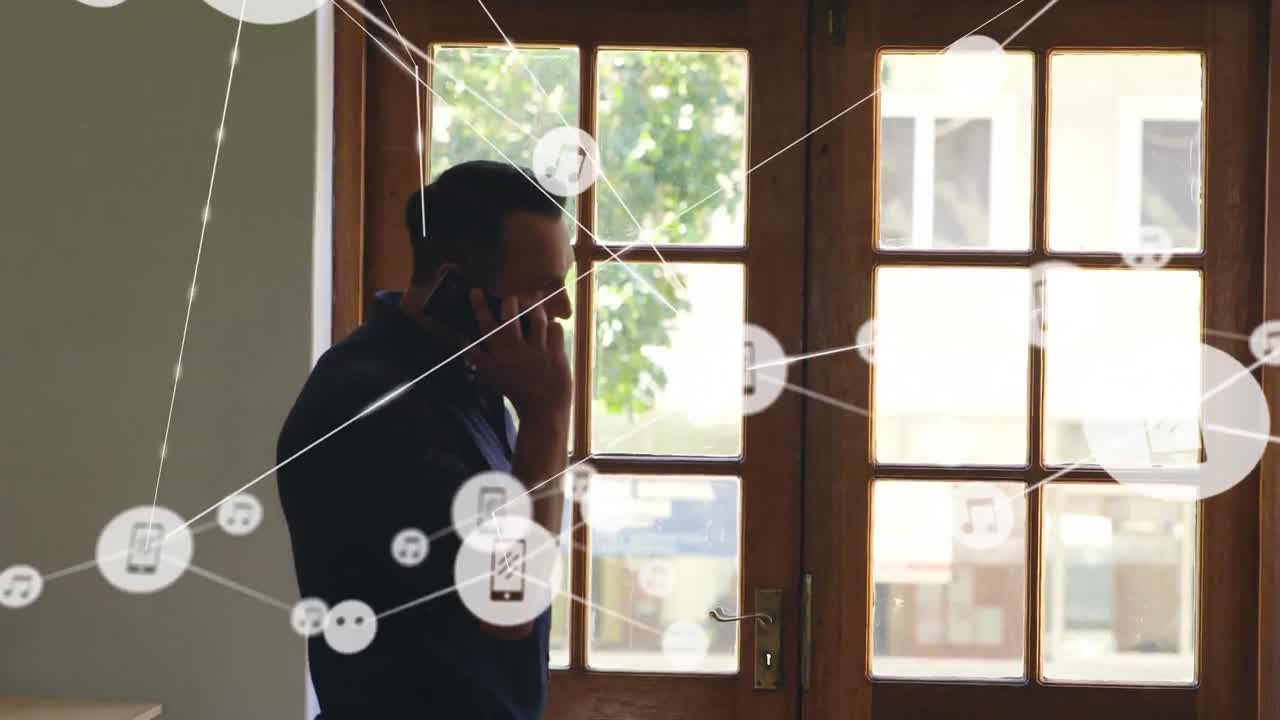 red de iconos digitales contra hombre caucásico hablando en teléfono inteligente cerca de la ventana en casa